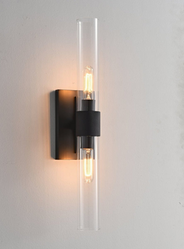 "A modern brass wall lamp with a long, vertical cylindrical glass shade, showcasing a bronze finish with black accents, blending vintage and contemporary styles."