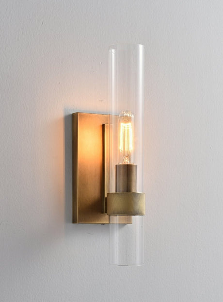 "A modern brass wall lamp with a cylindrical glass shade, blending vintage and contemporary styles with a bronze finish and black accents."