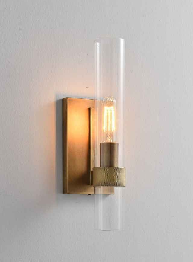 "A modern brass wall lamp with a cylindrical glass shade, blending vintage and contemporary styles with a bronze finish and black accents."