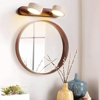 "A two-light travertine and dark wood vanity light mounted above a round mirror in a modern bathroom."