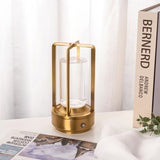 Orena Table Lamp - Sleek Rechargeable Indoor/Outdoor Light in gold, displayed on a white desk near books and curtains for modern decor.