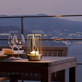 Orena Table Lamp - Sleek Rechargeable Indoor/Outdoor Light in gold, enhancing outdoor dining ambiance with warm LED on a balcony table.