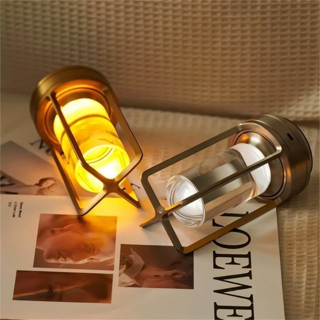 Orena Table Lamp - Sleek Rechargeable Indoor/Outdoor Light in gold, shown in warm and cool LED modes lying on a magazine surface.