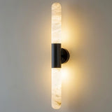 "Modern vertical wall lamp with a black metallic center and cylindrical alabaster shades emitting soft light."