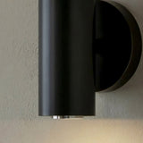 "Modern black wall lamp with a cylindrical design emitting a soft, downward light."