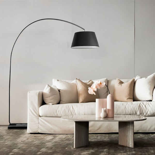 "A modern arc floor lamp with a black metal frame and a black fabric shade stands next to a white sofa in a living room setting."
