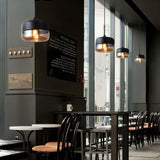 "Modern pendant lights with amber glass shades hanging in a cafe with dark walls and furniture."