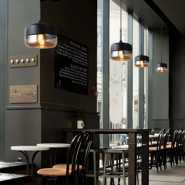 "Modern pendant lights with amber glass shades hanging in a cafe with dark walls and furniture."