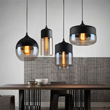 "Four modern pendant lights with different shaped glass shades hanging above a dining table."