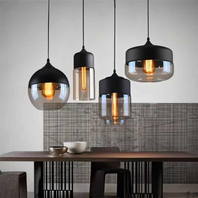 "Four modern pendant lights with different shaped glass shades hanging above a dining table."