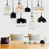 "A collection of modern pendant lights with various shapes and glass shades hanging above a dining table."