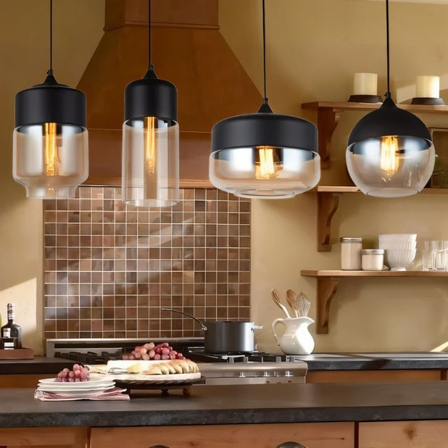 "Four modern pendant lights with different shaped glass shades hanging above a kitchen counter."