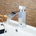Chrome single-handle waterfall bathroom faucet with white sink basin against wood brick tile background.