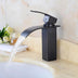 Black waterfall bathroom sink faucet with curved spout actively running water over a cream marble countertop.