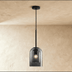 Clear glass pendant light with cylindrical shade, brushed metal hardware, suspended from ceiling canopy, white background, fr