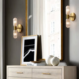 "Two modern brass wall lamps with textured glass shades in a hallway with a mirror and artwork."