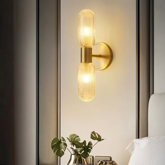 "A modern brass wall lamp with textured glass shades on a wall above a nightstand."