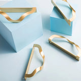 "Lifestyle image showcasing brass drawer pulls with an elegant, wavy design on light blue and white surfaces, suitable for modern or transitional interiors."