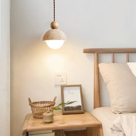 "A Palermo pendant light, made of yellow travertine with a wood accent, illuminates a modern bedside table in a softly lit bedroom."