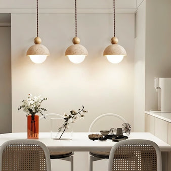 "Three Palermo pendant lights, made of yellow travertine with wood accents, hang above a dining table, creating a warm and inviting atmosphere."