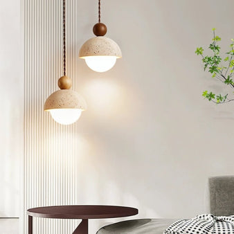 "Two Palermo pendant lights, made of yellow travertine with wood accents, hang above a round table, providing warm, ambient light in a modern living space."