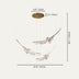 Brass feather chandelier with three suspended sculptural elements against a beige background.