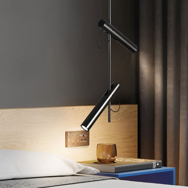 "A modern black stainless steel pendant light with adjustable tubes above a bedside table."