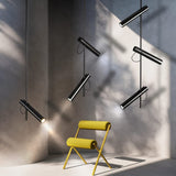 "Multiple modern black stainless steel pendant lights with adjustable tubes in a room with a yellow chair."