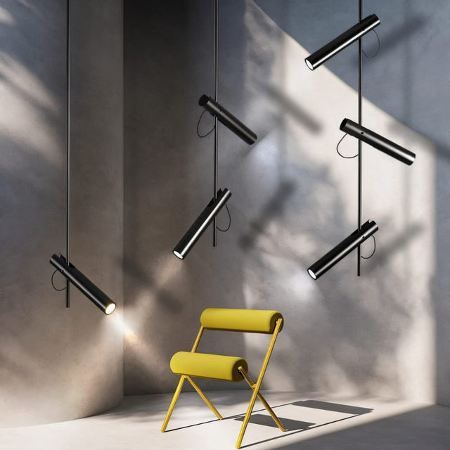 "Multiple modern black stainless steel pendant lights with adjustable tubes in a room with a yellow chair."