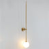 Brass wall lamp with long stem and illuminated frosted globe on white wall.