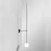 Minimalist wall-mounted pendant lamp with black metal frame and white spherical globe against white background.