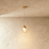 Two teardrop pendant lights with champagne metallic finish hang against white paneled wall above side table with sculptural v