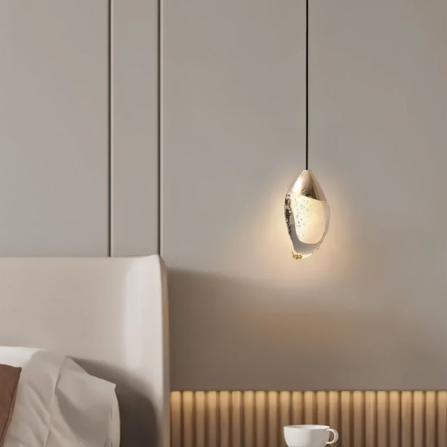 "Modern pendant light with a fluid crystal form and metal top above a nightstand in a bedroom."
