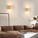 "A pair of modern, cube-shaped wall lamps made of yellow travertine, mounted on a neutral wall above a sofa in a living room, emitting a soft, ambient glow."