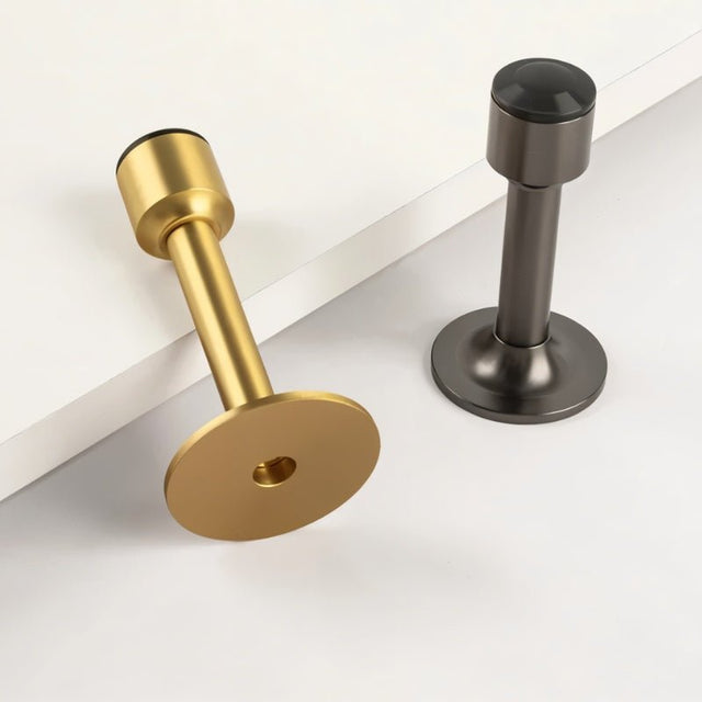 "Sculpted brass door stops with sleek, tapered silhouettes, polished finishes, wide stable bases, and magnetic holds in brass and gunmetal, designed to prevent wall damage."