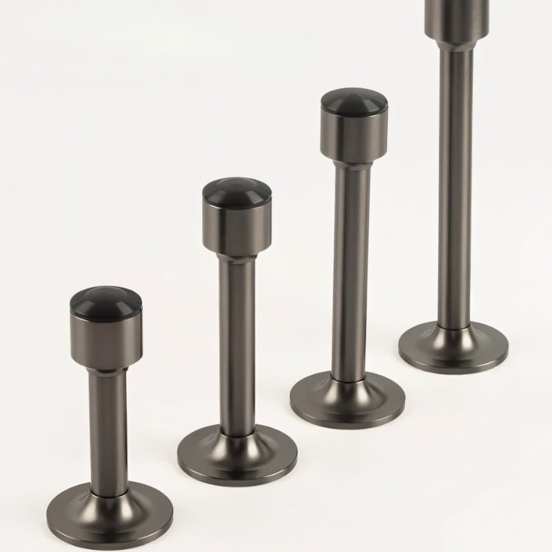 "Sculpted brass door stops with sleek, tapered silhouettes, polished finishes, wide stable bases, and magnetic holds in various modern finishes, designed to prevent wall damage."