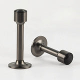 "Two sculpted brass door stops with sleek, tapered silhouettes, polished gunmetal finishes, wide stable bases, and magnetic holds, designed to prevent wall damage."