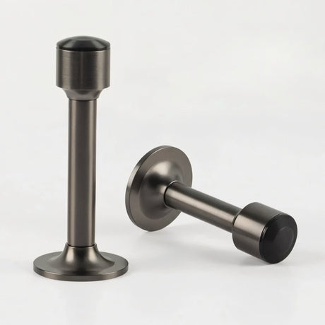 "Two sculpted brass door stops with sleek, tapered silhouettes, polished gunmetal finishes, wide stable bases, and magnetic holds, designed to prevent wall damage."
