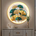 Posy Illuminated Art features a circular design with golden and teal ginkgo leaves, set against a soft, neutral wall.