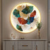 Illuminated circular wall art featuring multicolored ginkgo leaves, set against a plain beige wall background.
