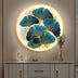 Illuminated art piece featuring teal and gold ginkgo leaves, mounted on a neutral wall next to a decorative vase and sculptur