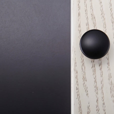 "A black dome-shaped brass cabinet knob with a flared base mounted on a two-tone cabinet, showcasing its simple elegance."