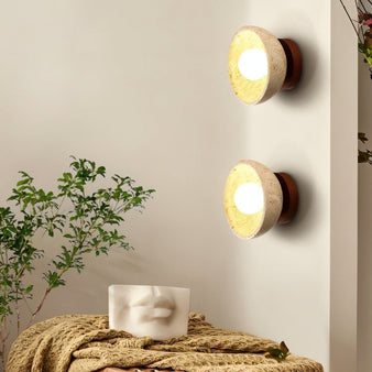 "Pair of travertine wall lamps with a circular wooden backplate, providing soft lighting in a bedroom setting."