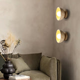 "Pair of travertine wall lamps with circular wooden backplates, illuminating a living room with a comfortable sofa."