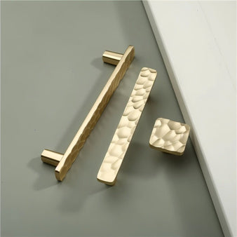 "Gold hammered texture cabinet knobs and pull bar handles, combining modern and artisanal design."