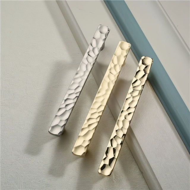 "Hammered texture pull bar handles in various metallic finishes, combining sleek lines with an artisanal appeal."