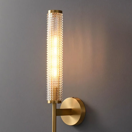 "Close-up of a modern brass wall lamp with a textured cylindrical glass shade."