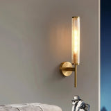 "A modern brass wall lamp with a textured glass shade casting a warm light on a gray wall."