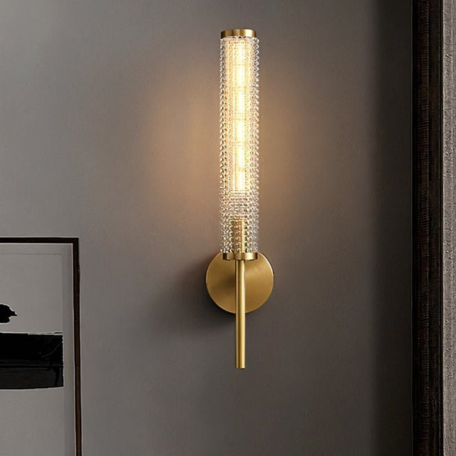 "A modern brass wall lamp with a textured glass shade on a gray wall."