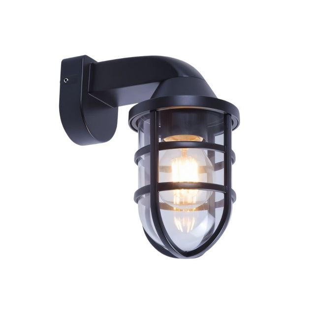 "A brass-colored, industrial-style wall lamp with a robust cage structure and clear PC diffuser, mounted on a stone wall, illuminating a garden path at night."